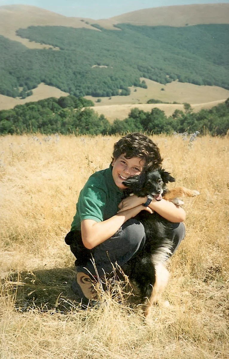 Carlo Acutis im grünen Poloshirt mit einem Hund auf einer Wiese